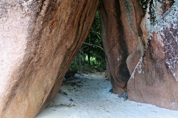 Obraz premium A narrow passageway between large rocks leading to a sandy area surrounded by greenery.