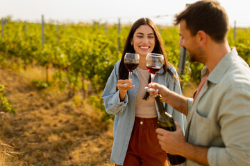 A joyful couple enjoying wine tasting together in a sunny vineyard during the golden hour, surrounded by lush green grapevines