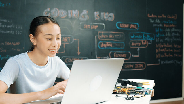 Smart girl programing system by using laptop at blackboard. Highschool student writing engineering code or prompt while looking at screen at STEM technology class. Creative education. Edification.