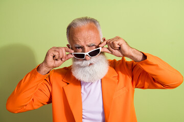 Portrait of aged man performer arms touch sunglass look wear orange suit isolated on green color background