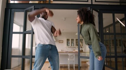 African American happy family love couple laugh woman man guy girl jumping on couch sofa at own home energetic dance jump together cheerful husband wife celebrate moving day fun fooling dancing music