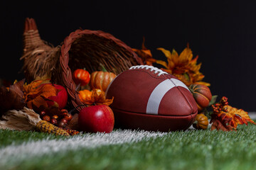 Low angle selective focus view of a cornucopia and football surrounded by harvest fruits and vegetables