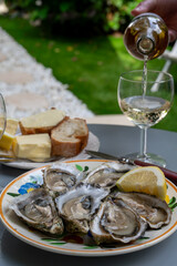 Plate with fresh live oysters with citron, bread, butter and white wine served at restaurant in oyster-farming village, Arcachon bay, Gujan-Mestras port, France
