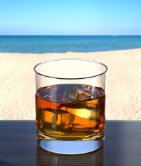 Glass of cognac on the wooden table in the beach bar. Picturesque background with sand and sea. Glassware with the drink. 3d rendering.