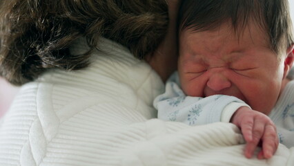 Newborn crying while being held close by grandmother, capturing a moment of distress and comfort,...