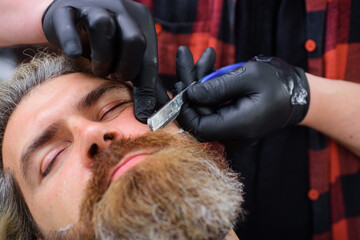 Bearded man in barbershop. Hairstylist serving client at barber shop. Professional beard care. Straight razor, barber shop. Vintage barbershop, shaving. Man hairstylist. Bearded man. Closeup portrait.