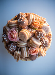 Decorating a birthday cake with macarons, chocolate balls, and flowers against a blue backdrop