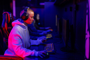 Side view of gamer girl playing online video games in gaming room.