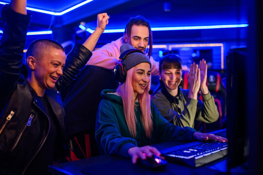 Gamer girl playing a video game in cybercafe while friends cheering.