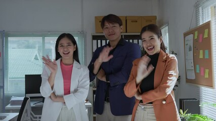 Three young asian managers pose together in an office, smiling and waving at the camera. Their cheerful expressions reflect a positive and welcoming workplace atmosphere