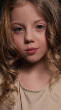 Portrait of a little sad girl on a dark background. Vertical video.
