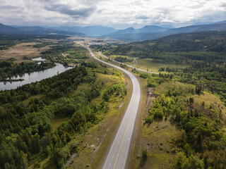 Scenic Aerial View of a Tranquil Road Winding Through Lush Green Forests and Hills in Alberta, Canada