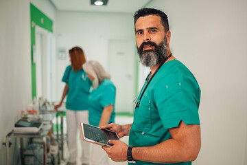 Male nurse with tablet in hospital hallway, looking forward.