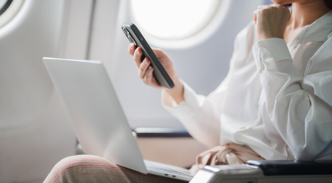 In-Flight Productivity: Businesswoman manages her tasks seamlessly, working on laptop and smartphone amidst air travel. - Powered by Adobe