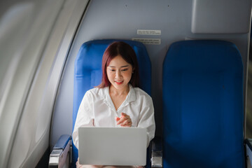 In-Flight Productivity: Young Asian businesswoman working on laptop in airplane seat. 