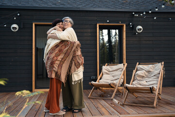 Couple of senior adult asian women hugging outdoors in front of country house