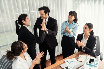 Group of happy businesspeople in high five gesture and successful efficient teamwork. Diverse race office worker celebrate after made progress on marketing planning in corporate office. Meticulous