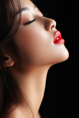 Fototapeta premium A close-up of a woman's face with glossy skin, closed eyes, and striking red lips, capturing beauty and elegance against a dark background.