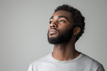 Obraz premium Young man gazing upward in a heather grey oversized cotton shirt against a neutral backdrop