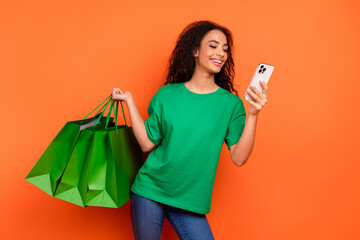 Photo of young happy girl using smartphone texting holding shopping bags order taxi to home isolated on orange color background © deagreez