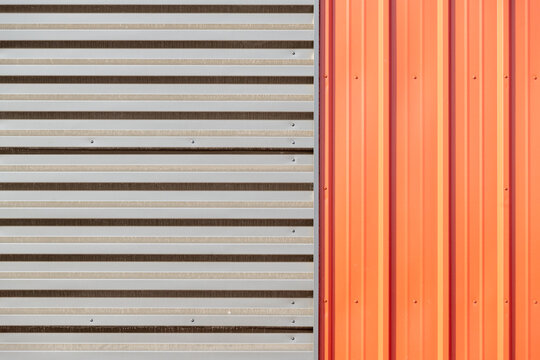 Grey and orange metal composite panels both horizontal and vertical. The aluminum cladding is on the exterior of a commercial building's wall. The bright colored covering is textured and shiny. 
