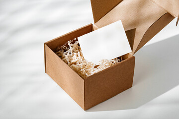 A simple brown gift box with natural filling sits elegantly on a light surface, capturing soft shadows