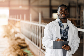 Smiling veterinarian in white lab coat holding clipboard inside cattle barn. Professional animal...
