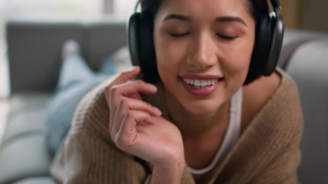 Hispanic latin woman relaxed girl Caucasian lady happy female lying on couch home apartment listen music headphones enjoy sound eyes closed sing song listening audio in earphones relax leisure smiling