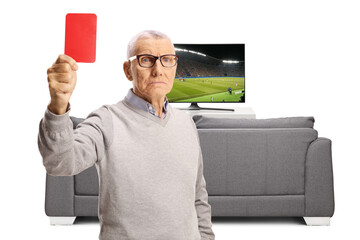 Serious elderly man showing a red card in front of tv and sofa