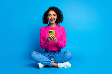 Full body photo of attractive young woman sit floor hold device dressed stylish pink clothes isolated on blue color background