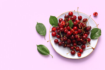 Plate with sweet cherries and leaves on lilac background