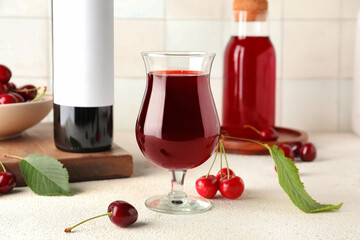 Glass and bottles of sweet cherry liqueur with berries on white table near tile wall