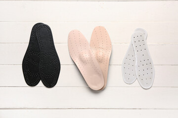 Set of different orthopedic insoles on light wooden background