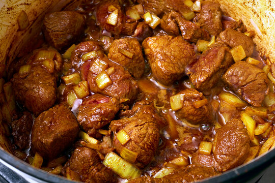 Pieces of lamb and onion browning in a Dutch Oven.