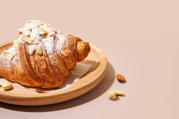 Wooden plate of sweet croissant with powdered sugar and different nuts on pink background