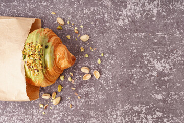 Paper bag with sweet croissant and pistachio nuts on dark table