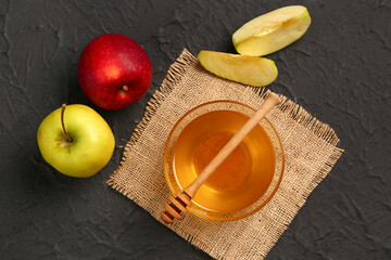 Glass bowl of sweet honey with apples and dipper on black background