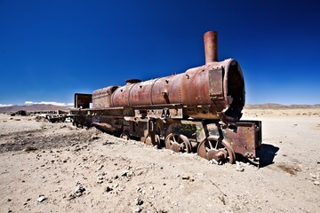 An abandoned, rusty steam locomotive in a barren landscape under a clear blue sky.