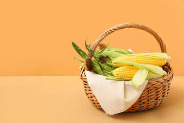 Wicker basket with fresh corn cobs on brown background