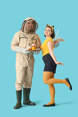Male beekeeper with honey and woman in bee costume on blue background