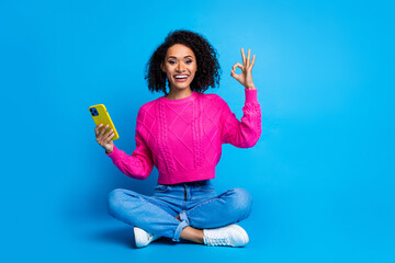 Full body photo of attractive young woman sit floor hold device okey dressed stylish pink clothes isolated on blue color background