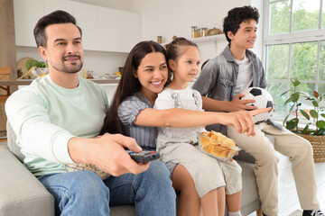 Happy family with TV remote control, snacks and soccer ball watching football game at home