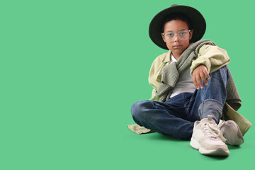 Little African-American boy in adult clothes sitting on green background