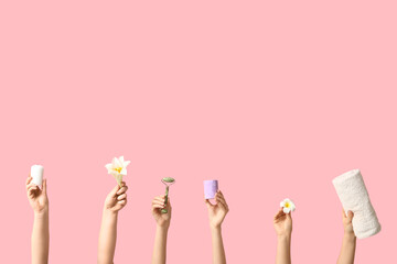 Female hands with flowers, candles, towel and facial massage tool on pink background