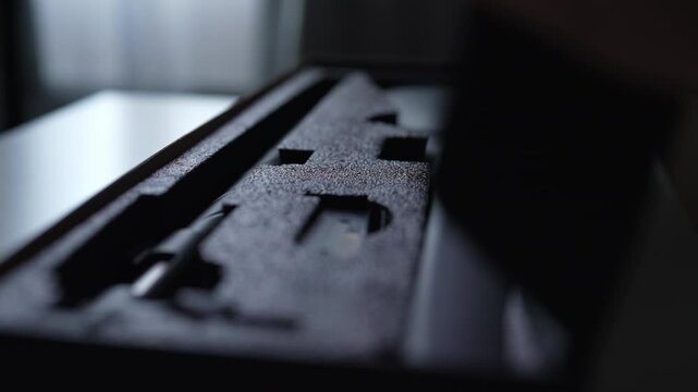 Closeup of unrecognizable hunter male opening gun case on white table reveals weapon along with accessories. Hard black plastic case features soft foam inserts for protection and secure storage.