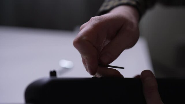 Closeup hands of unrecognizable gunsmith using key to tighten screws on rifle barrels, ensuring optimal maintenance and functionality. Technician conducting rifle maintenance employs precision tools.