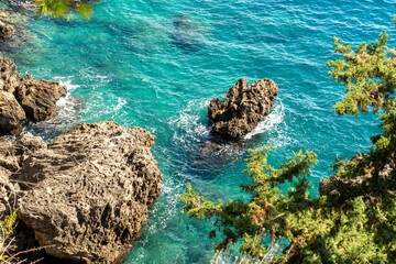 Sea waves hitting the high rocks in the deep blue sea and green vegetation
