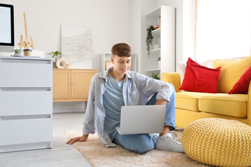 Young man using laptop on carpet at home