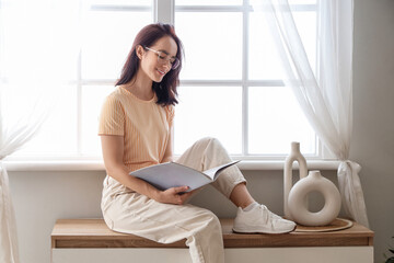 Young woman reading magazine on commode at home