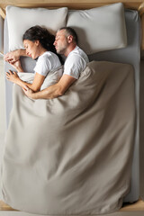 Bedtime. Spouses sleeping, lying on big bed and resting, husband embracing wife from back, top view, horizontal shot